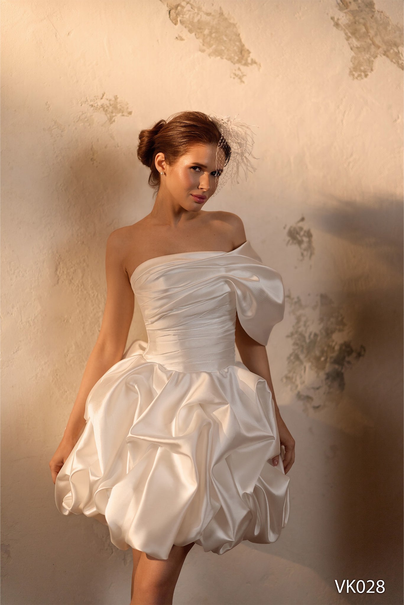 Modern bridal mini dress with asymmetrical off-shoulder neckline, sculptural draped bodice, voluminous bubble skirt, and lace-up back