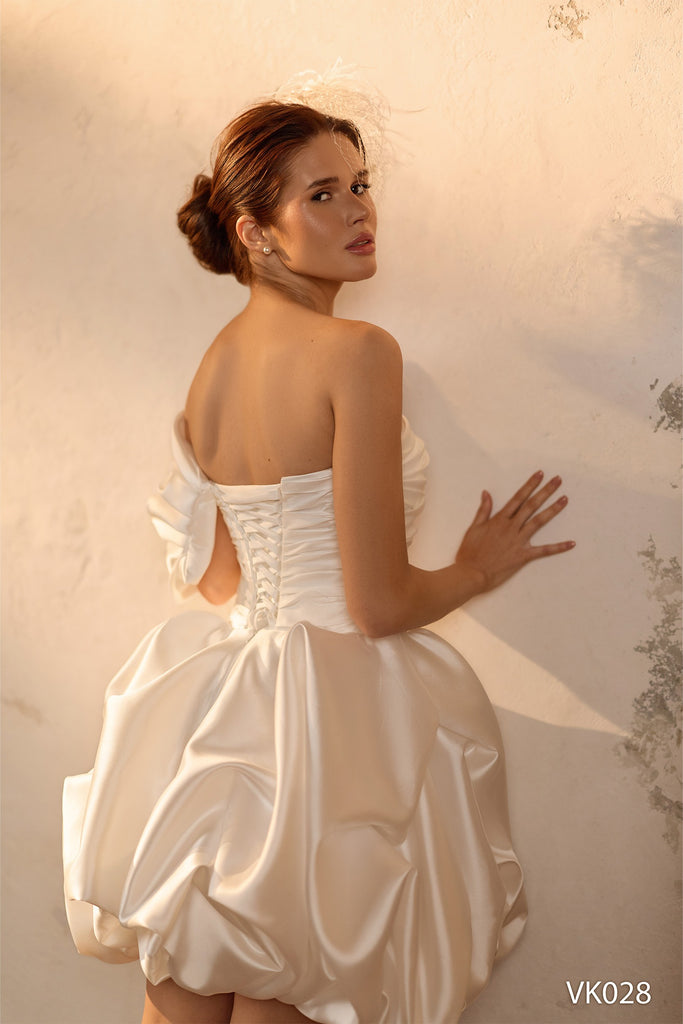 Modern bridal mini dress with asymmetrical off-shoulder neckline, sculptural draped bodice, voluminous bubble skirt, and lace-up back