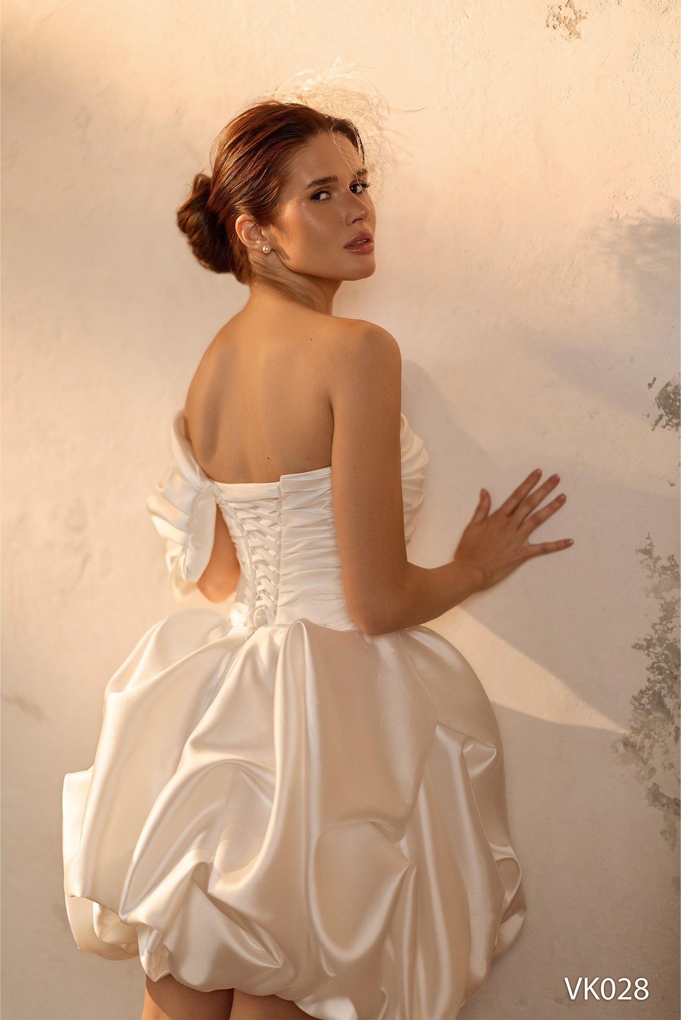 Modern bridal mini dress with asymmetrical off-shoulder neckline, sculptural draped bodice, voluminous bubble skirt, and lace-up back