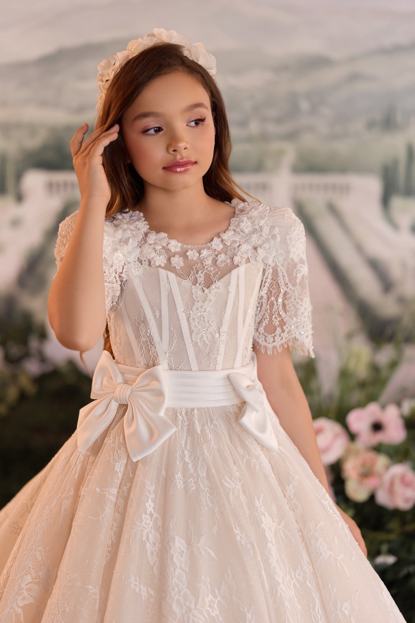 Girl wearing a white lace dress with a satin bow waist and floral headpiece