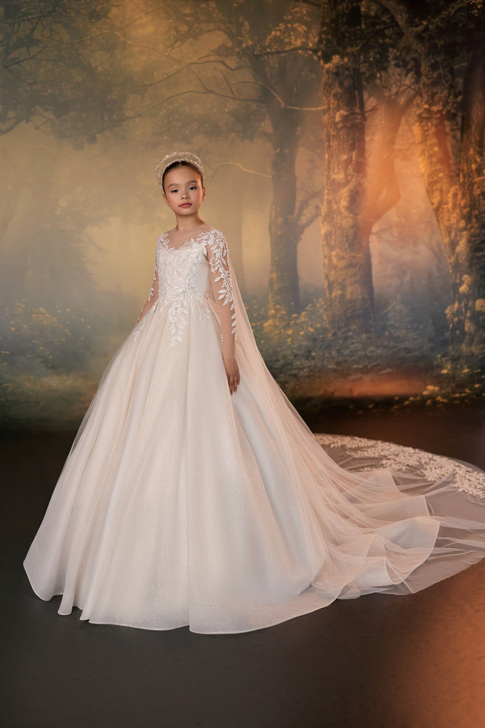 Girl wearing a white ball gown with lace sleeves and a long train against a forest background