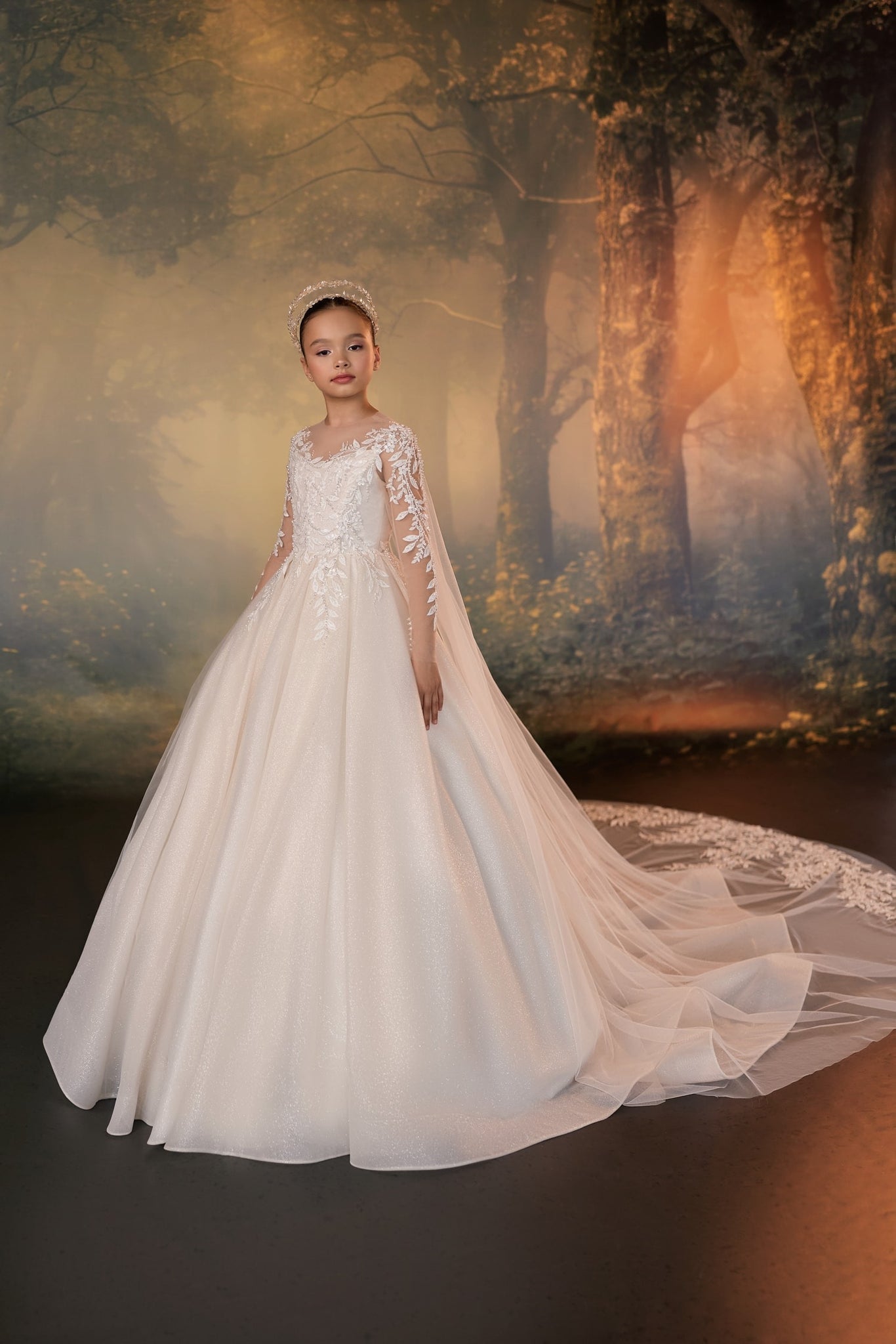 Girl wearing a white ball gown with lace sleeves and a long train against a forest background