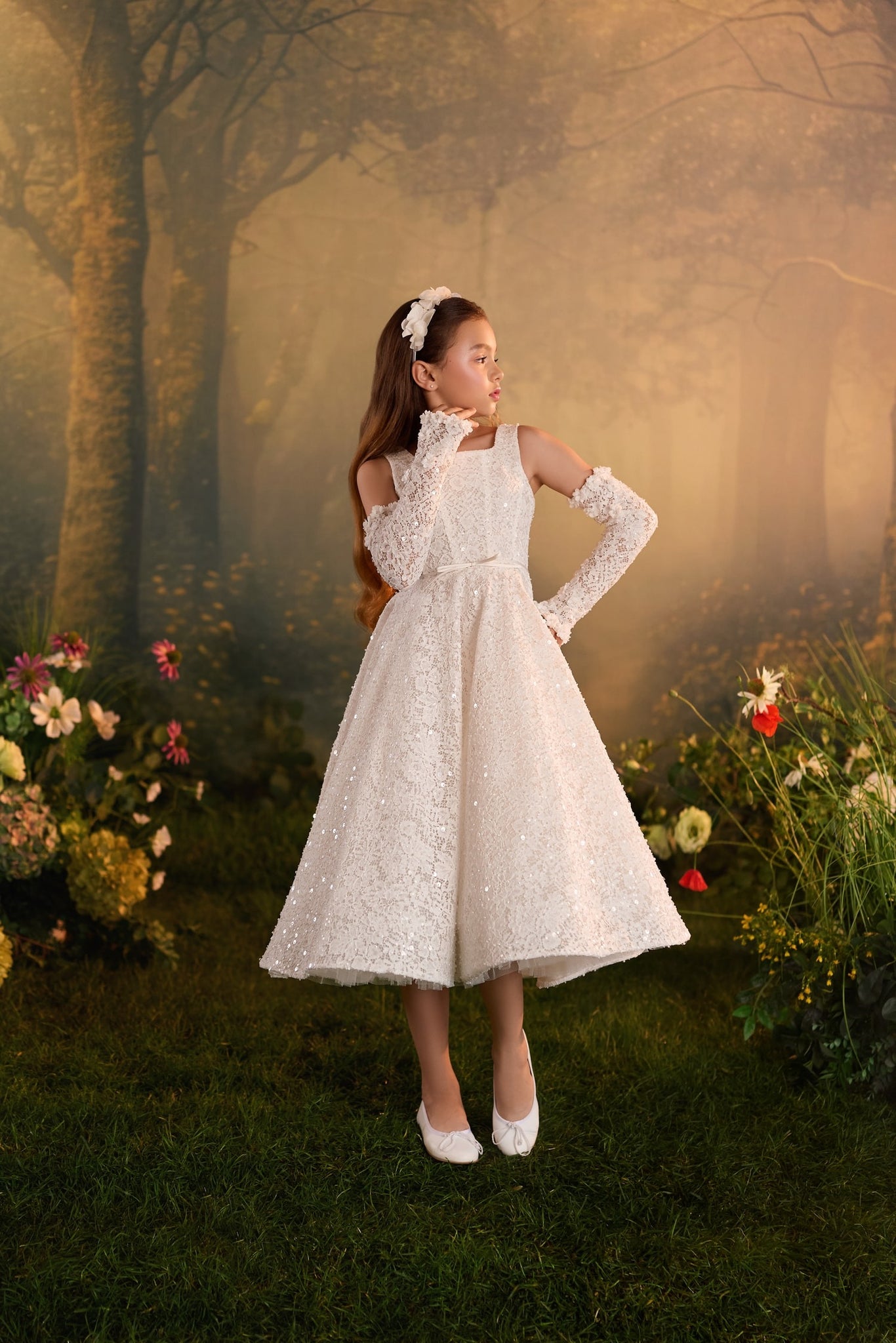 Girl wearing a white lace dress with matching gloves and a floral headband in a forest setting