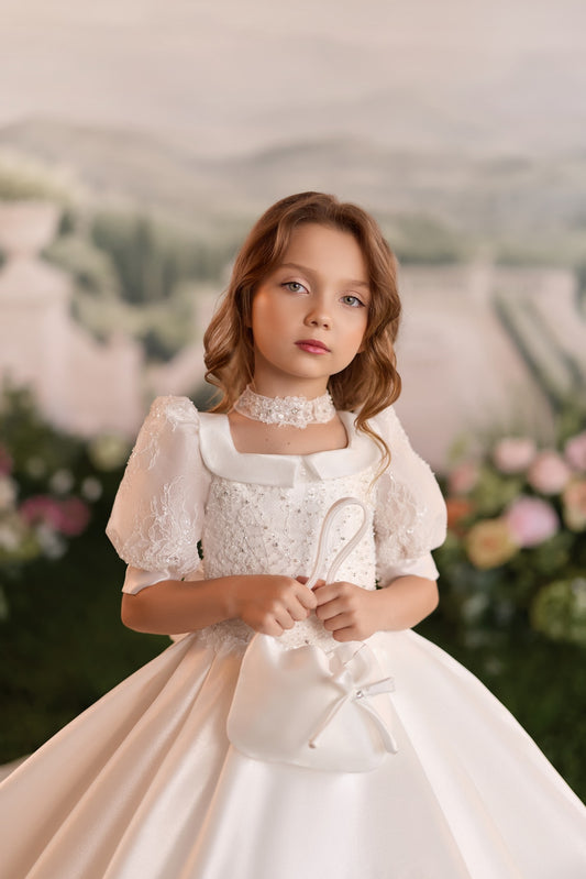 Girl wearing a white formal dress with puff sleeves and a matching lace choker holding a small white handbag