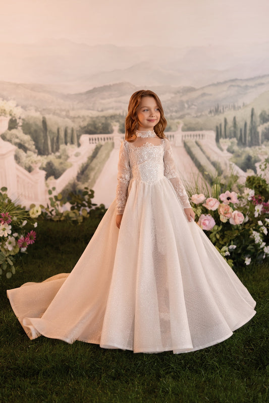 Girl wearing a long sleeve light cappuccino lace ball gown with a train standing in a garden setting