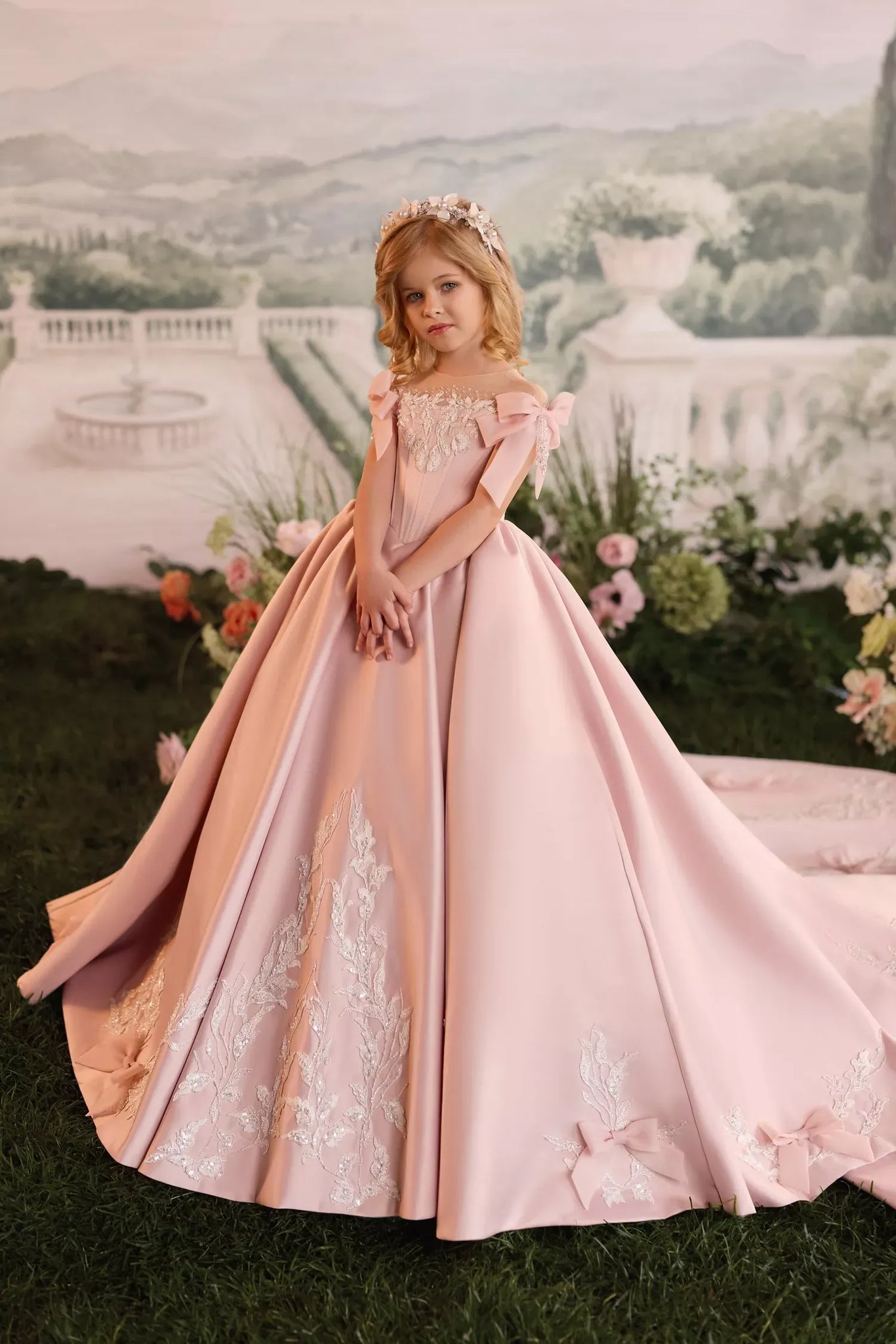 Girl wearing a pink ball gown with lace embroidery and bows standing in a garden