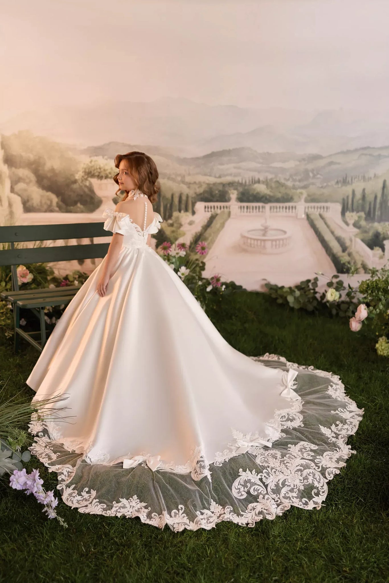 Girl wearing a white satin ball gown with a lace train and off shoulder sleeves