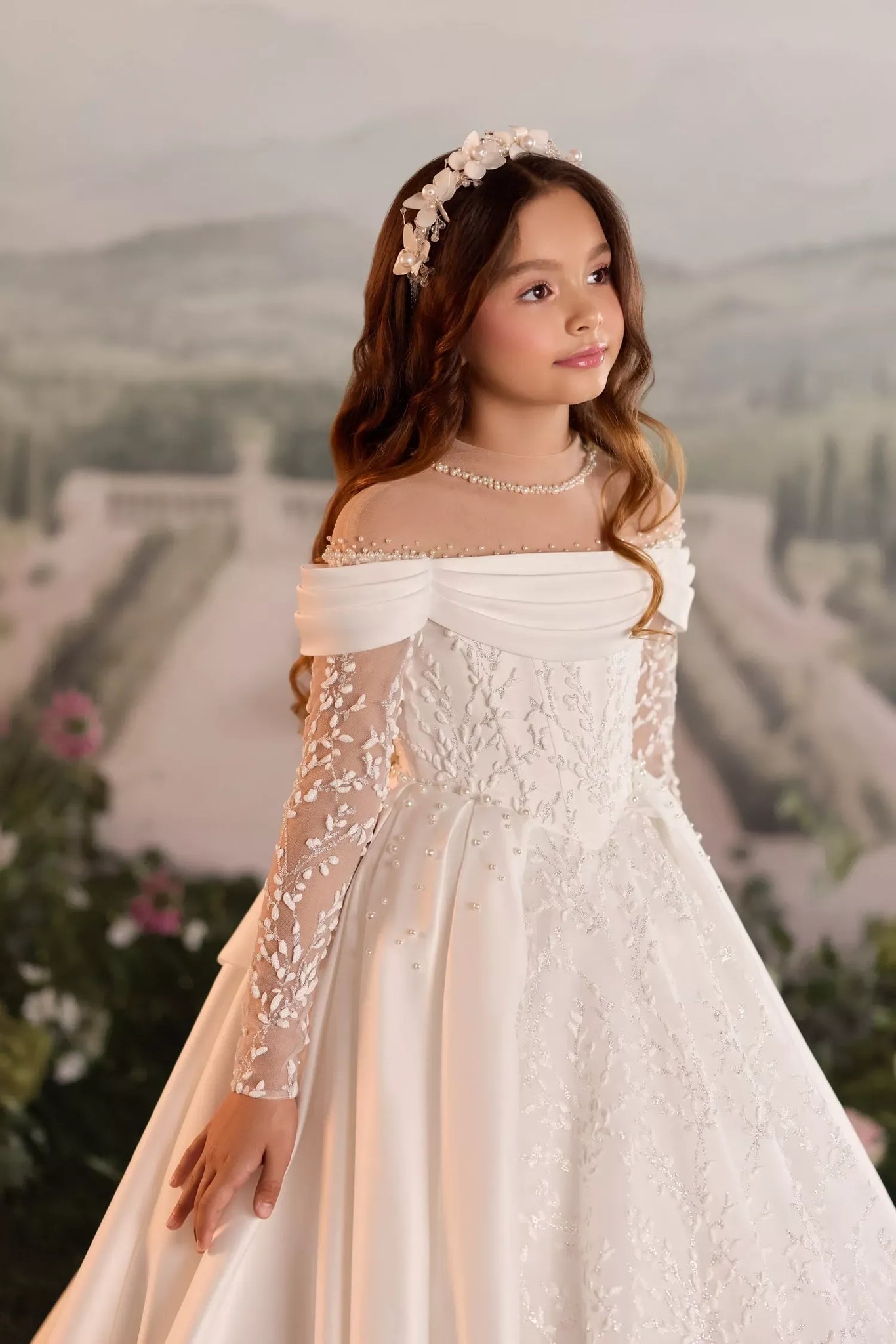 Girl wearing a white off the shoulder formal dress with long lace sleeves and a floral headpiece