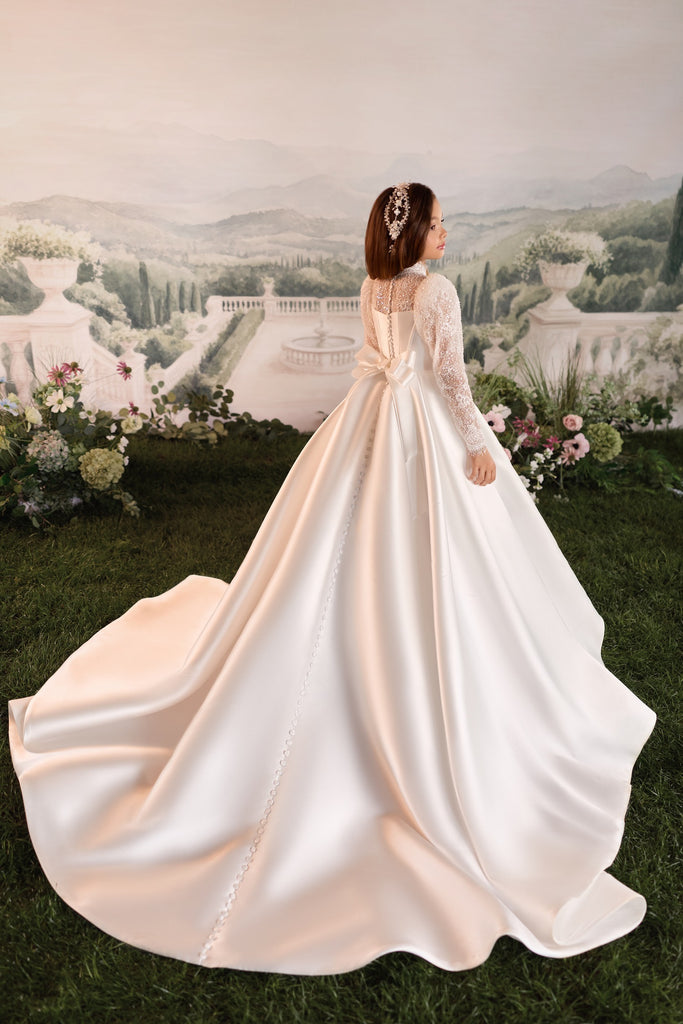 Back view of girl wearing a Mikado ball gown with long lace sleeves, sheer back detail, and a full skirt | Girls Formal Dress