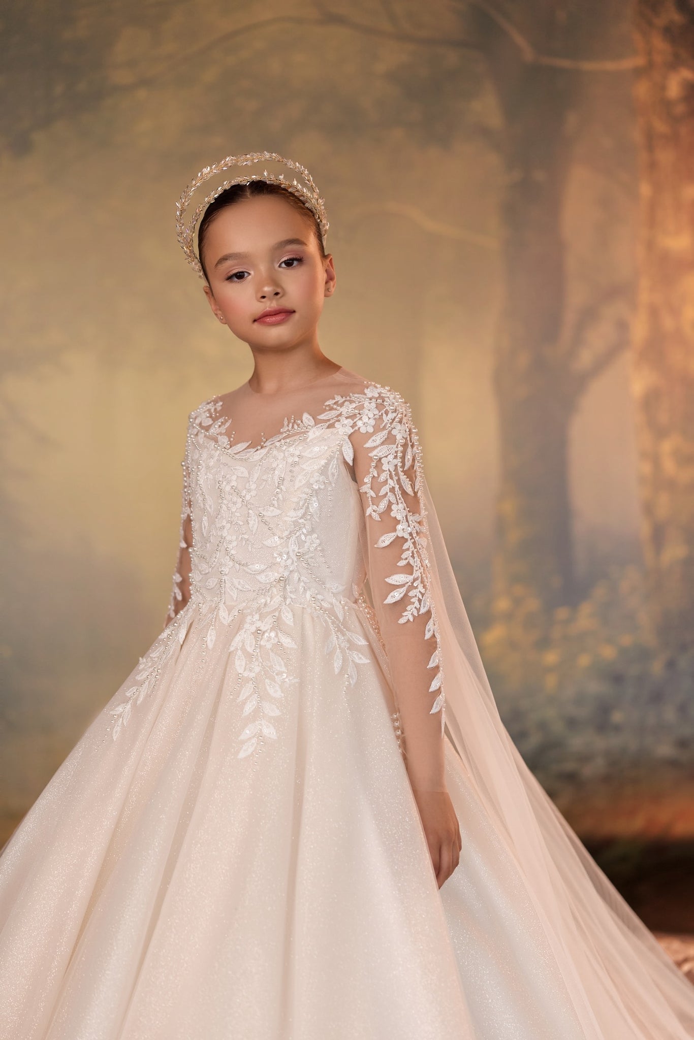 Girl wearing a white floral lace gown with long sleeves and a beaded headpiece