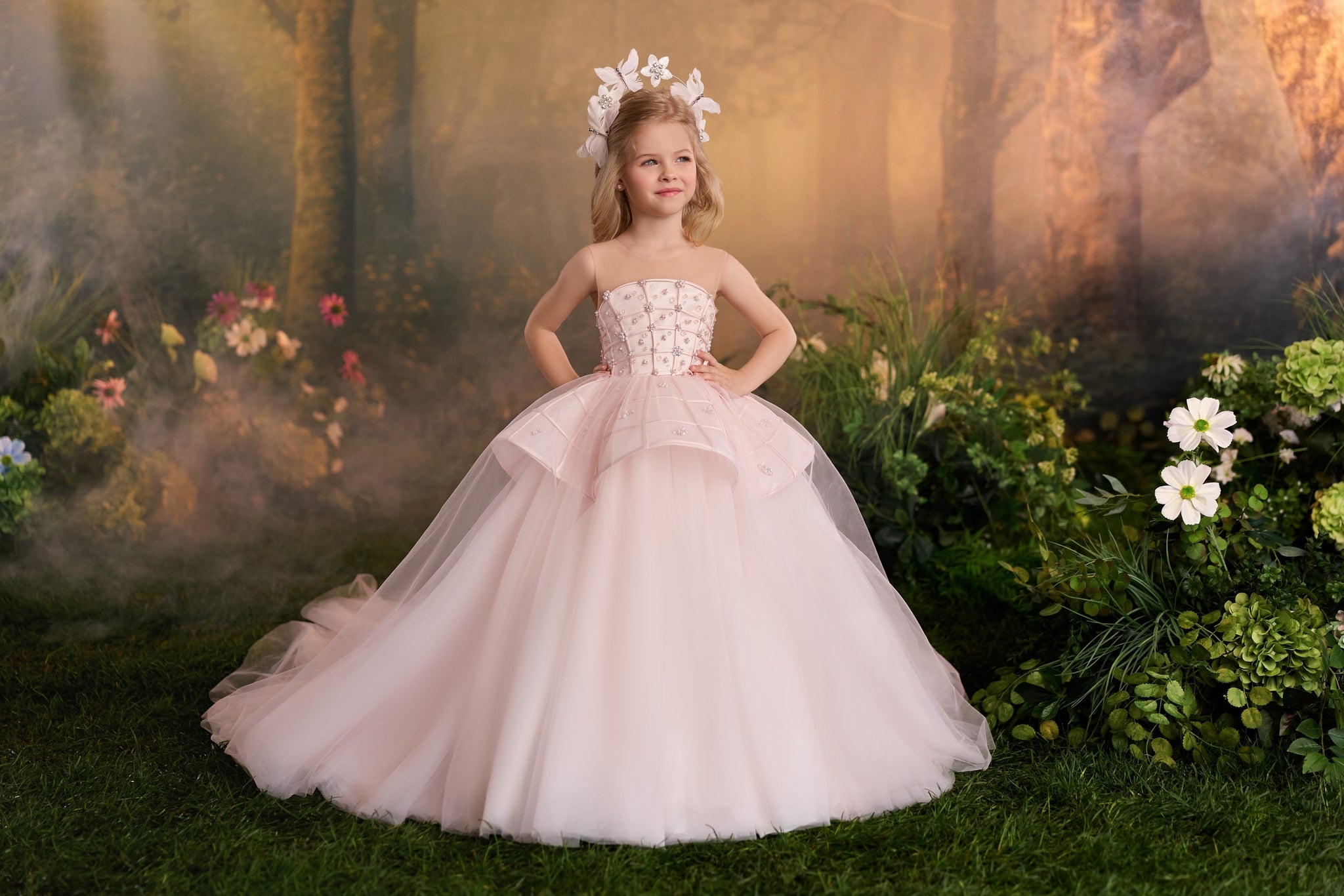 Girl wearing a pink ball gown with a floral headpiece standing in a garden setting