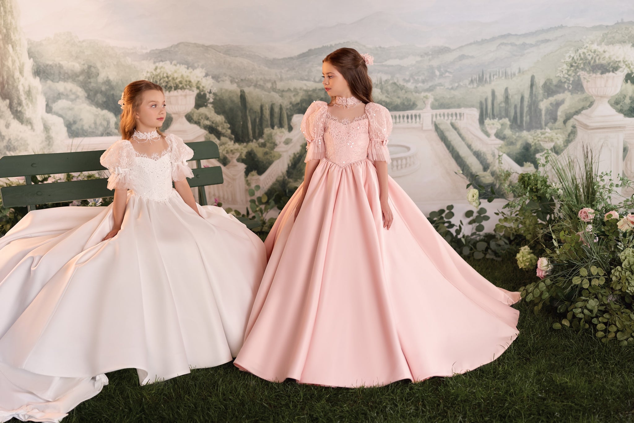 Two girls wearing formal ball gowns in a garden setting