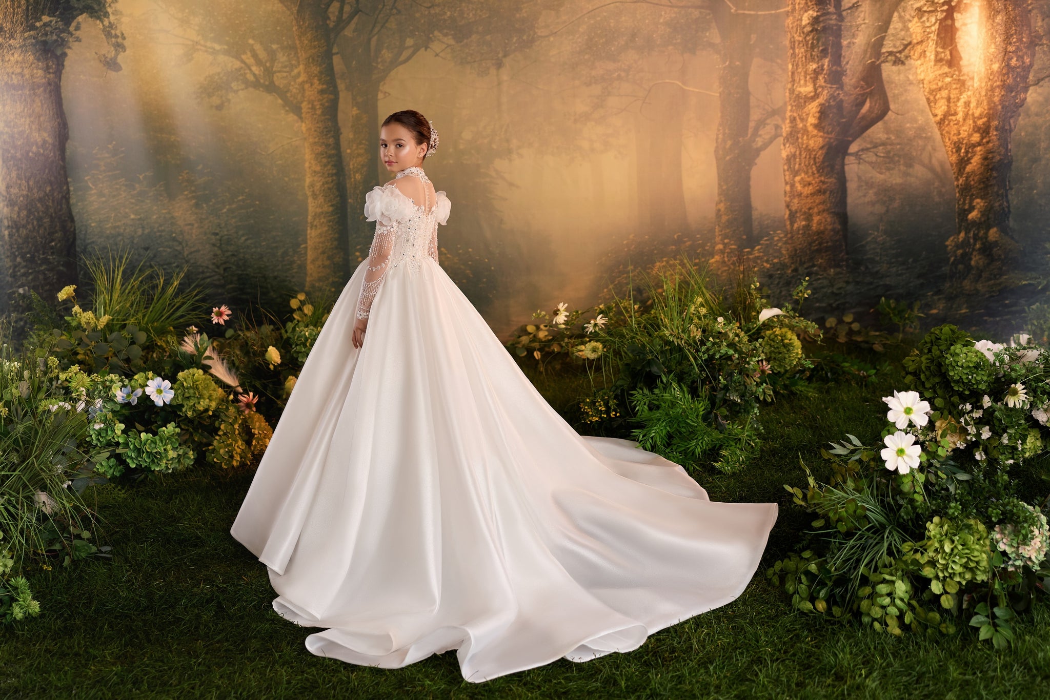 Girl wearing a white ball gown with lace sleeves and a long train standing in a forest setting