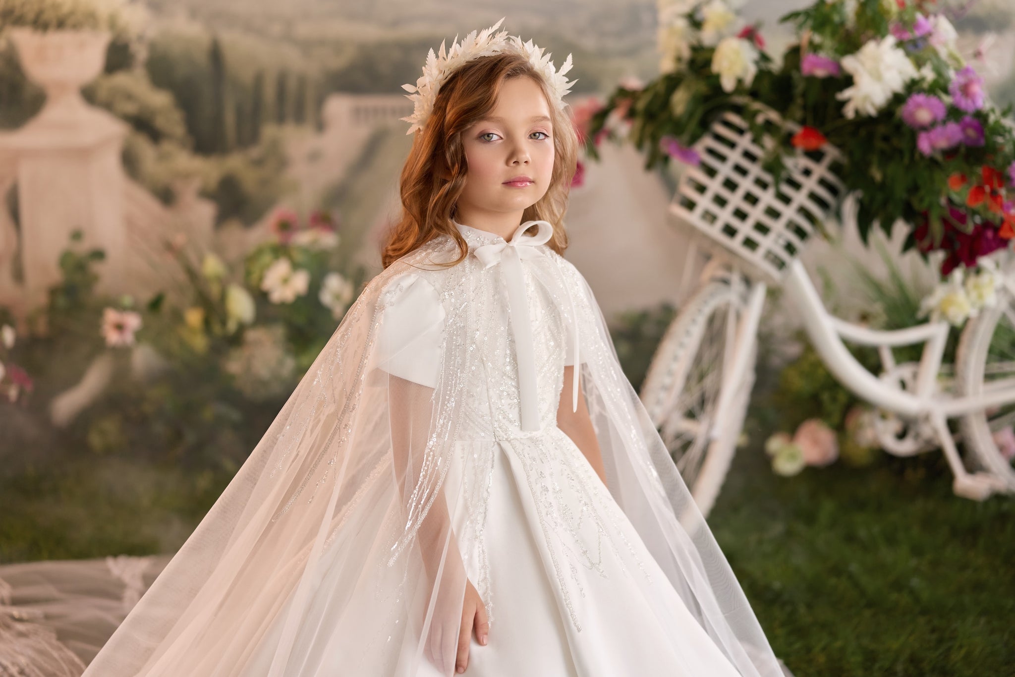 Girl wearing a white communion dress with a sequined cape and a floral headpiece