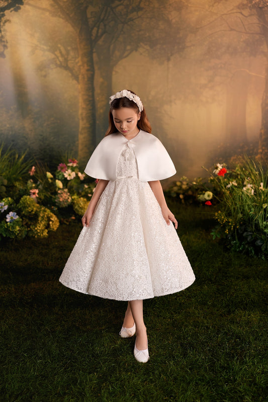 Girl wearing a white lace dress with a cape and floral headband in a garden setting