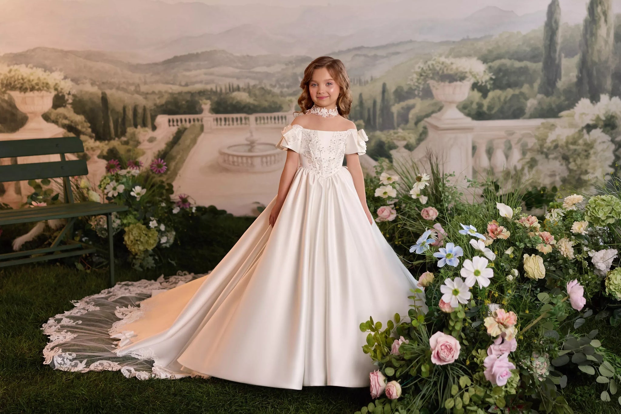 Girl wearing a white off-shoulder ball gown with lace detailing and a train in a garden setting
