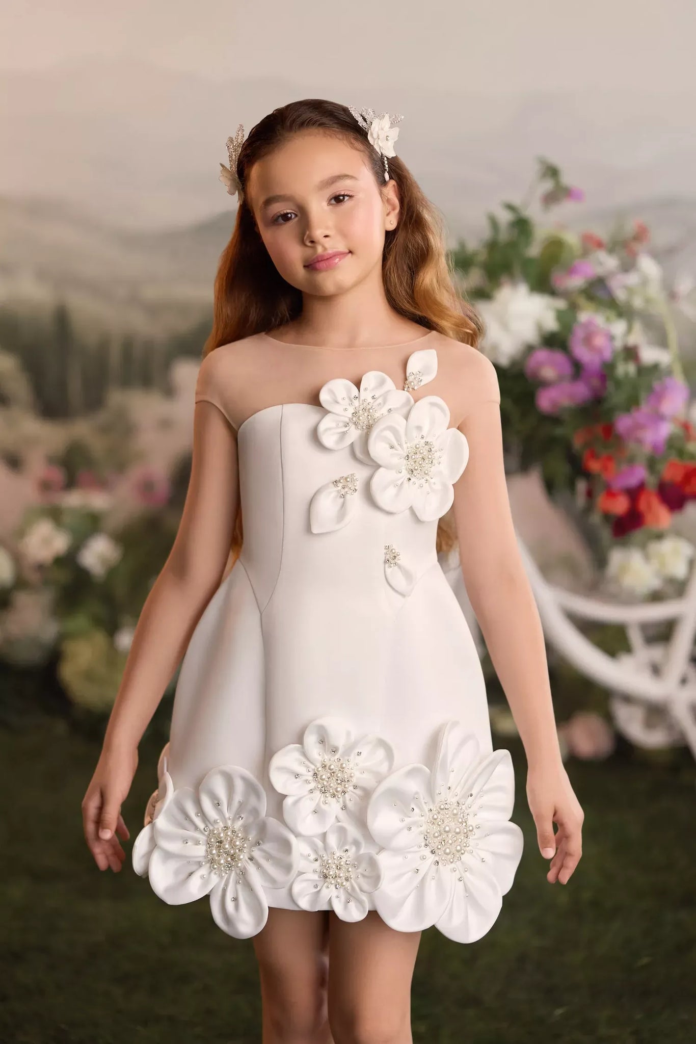 Girl wearing a white sleeveless dress with large fabric flower appliqués and pearl embellishments