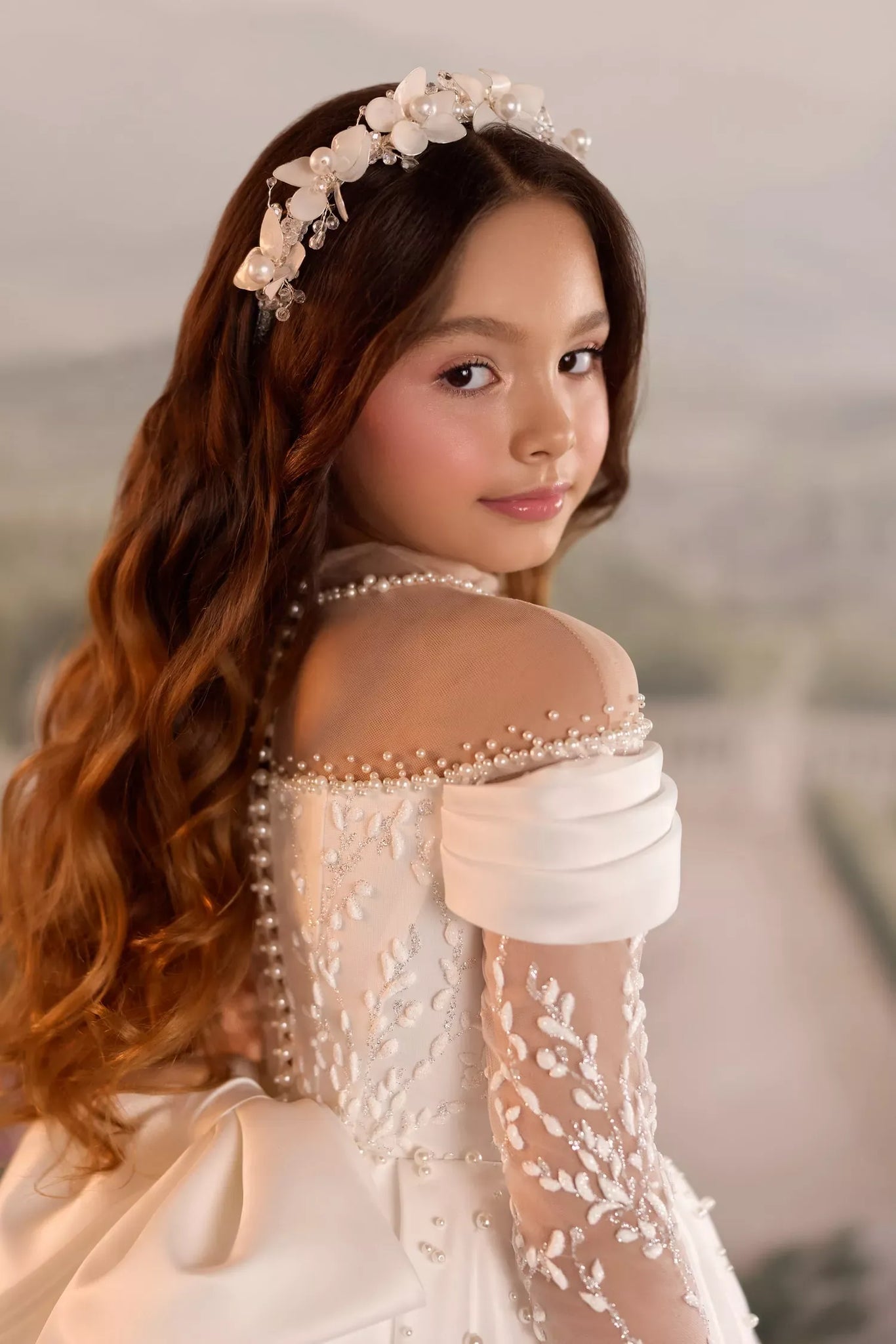 Girl wearing a white formal dress with pearl embellishments and a floral headpiece