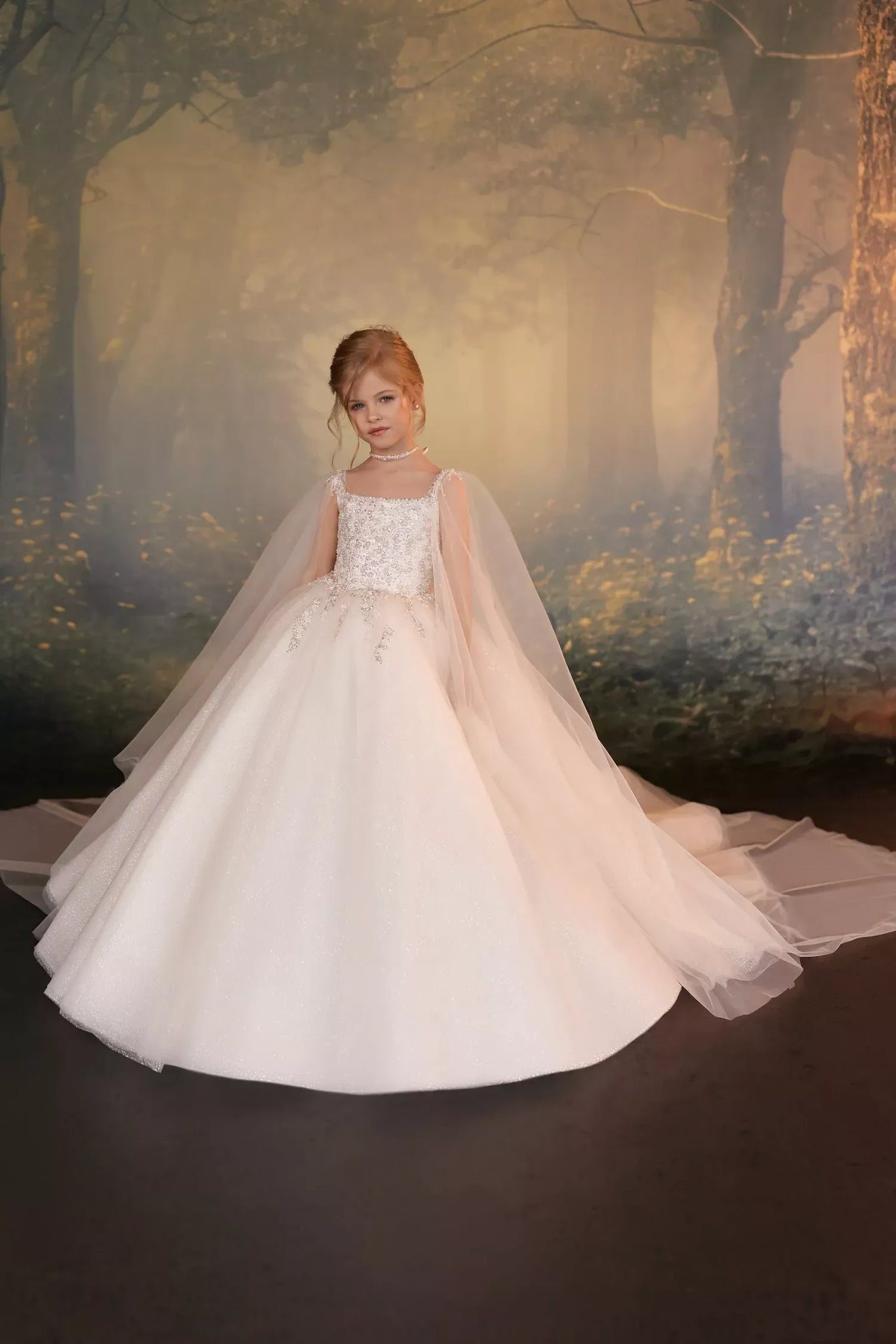 Girl wearing a white ball gown with a cape and beaded bodice against a forest backdrop