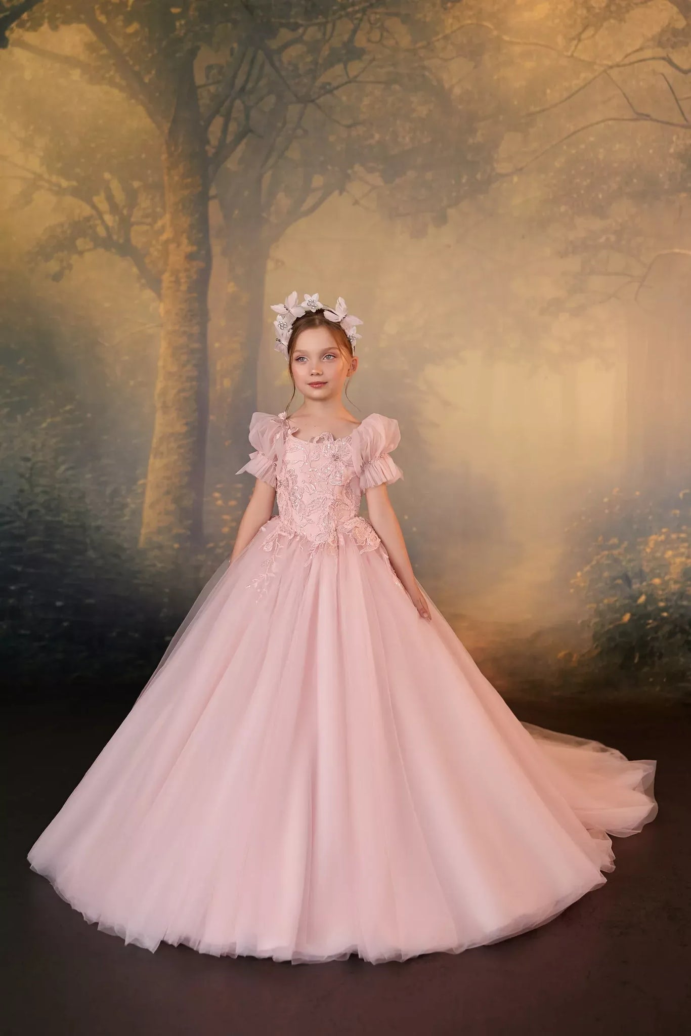 Girl wearing a pink tulle ball gown with floral embroidery and a matching headpiece