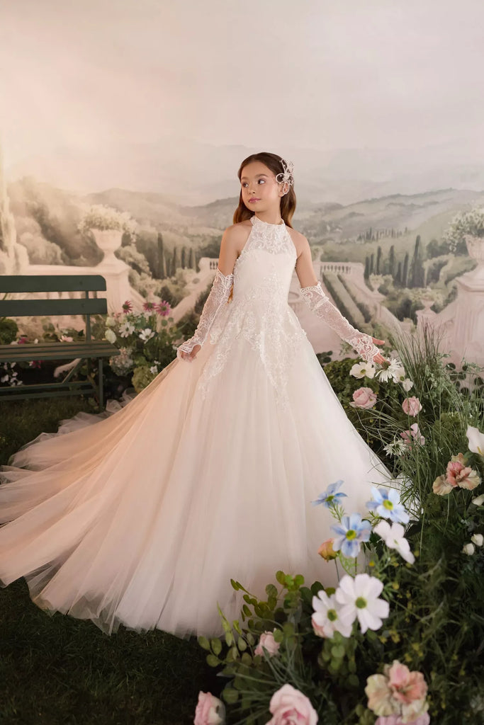 Girl wearing a white lace halter neck gown with matching lace sleeves standing in a garden setting | Girls Formal Dress