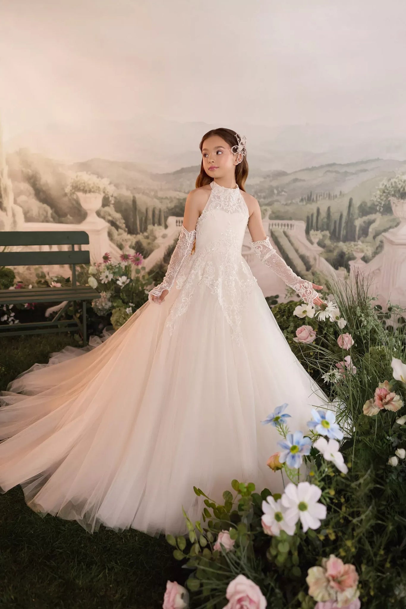 Girl wearing a white lace halter neck gown with matching lace sleeves standing in a garden setting | Girls Formal Dress