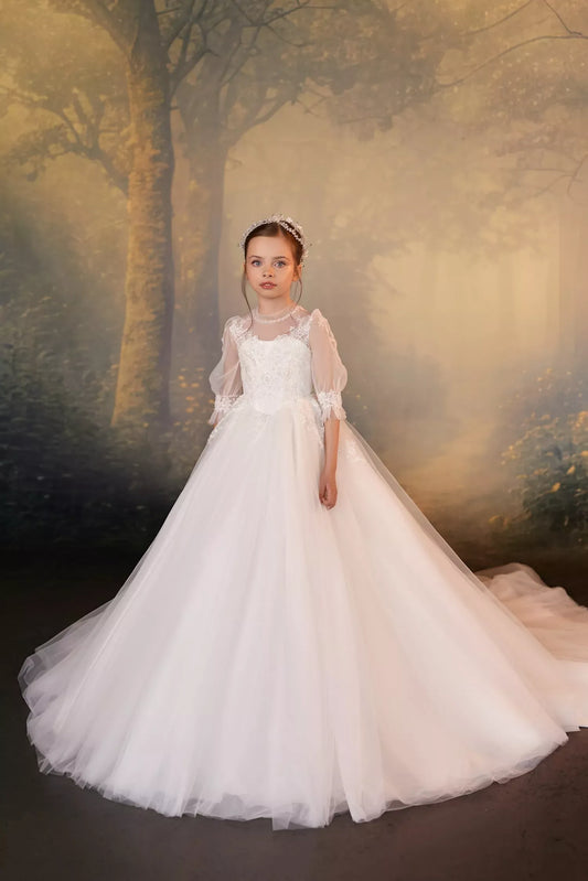 Girl wearing a white lace ball gown with puff sleeves and a crystal headpiece against a forest backdrop