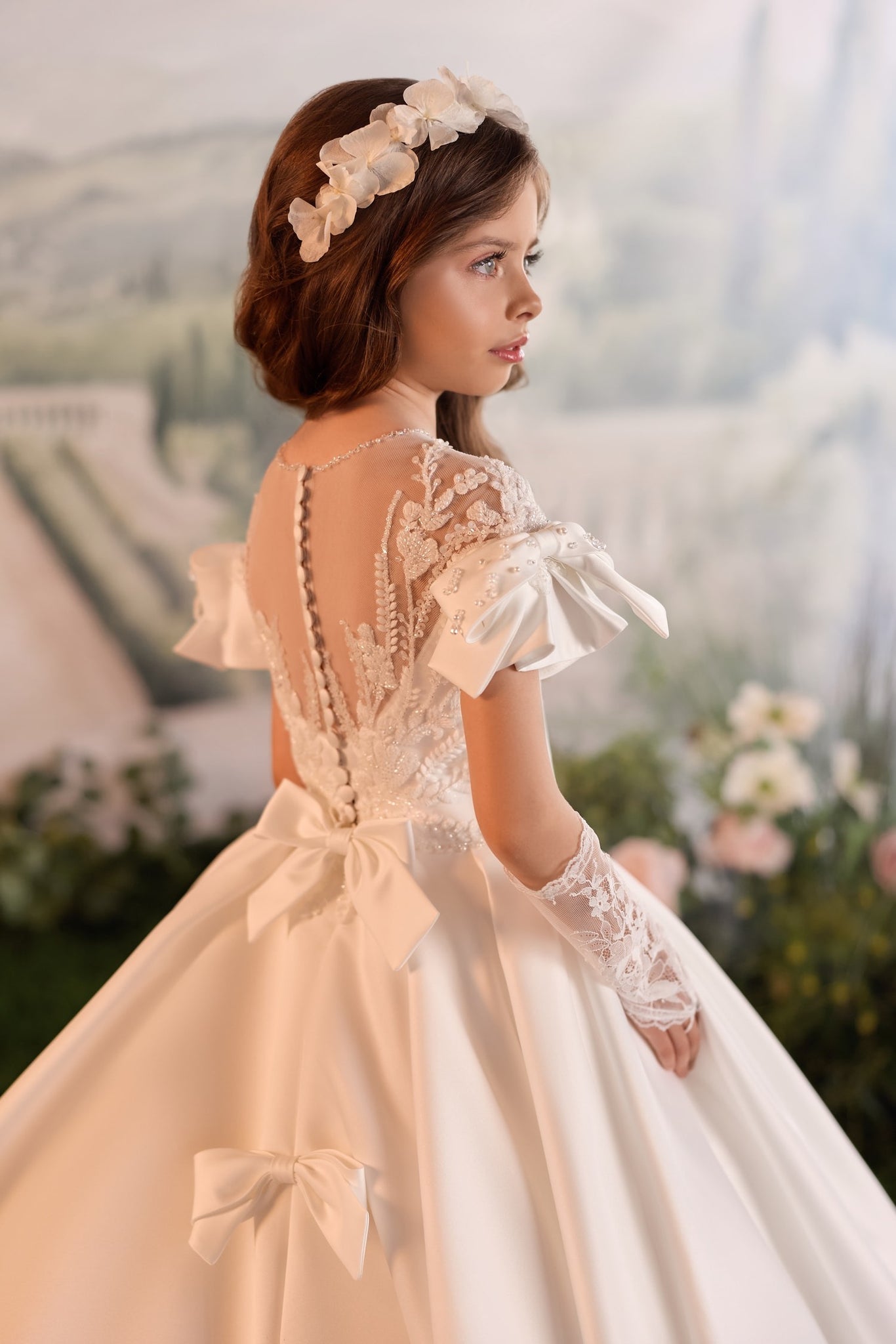 Girl wearing white lace communion dress with floral headband and lace gloves