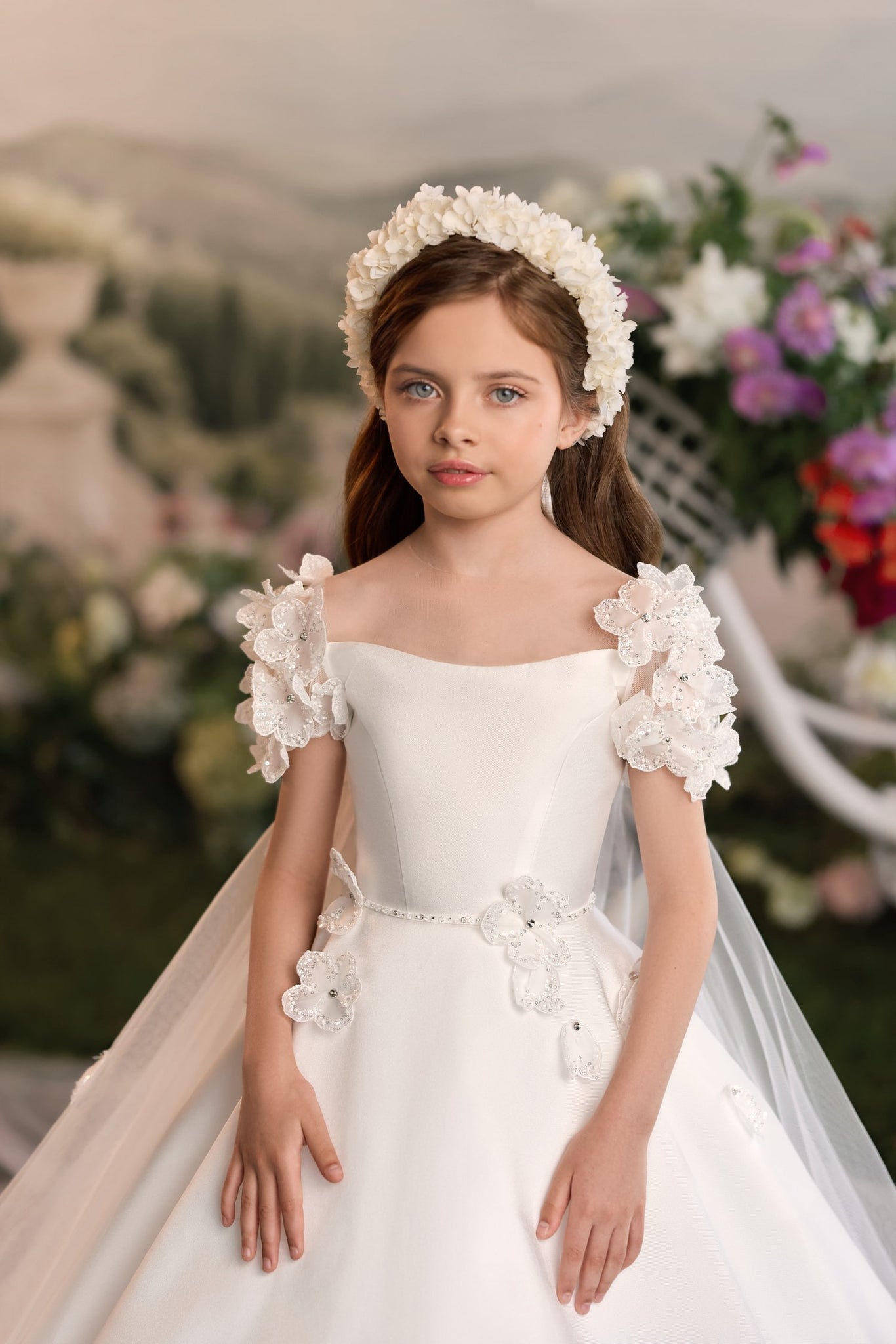 Girl wearing a white floral headband and a white dress with flower embellishments on the sleeves and waist