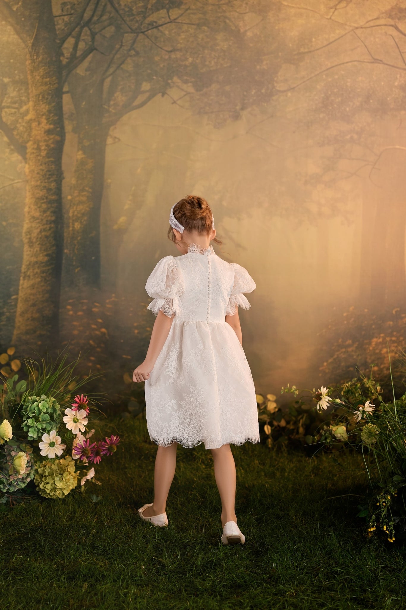 Child seen from behind wearing a white lace dress with puff sleeves standing in a misty forest setting | Girls Formal Dress