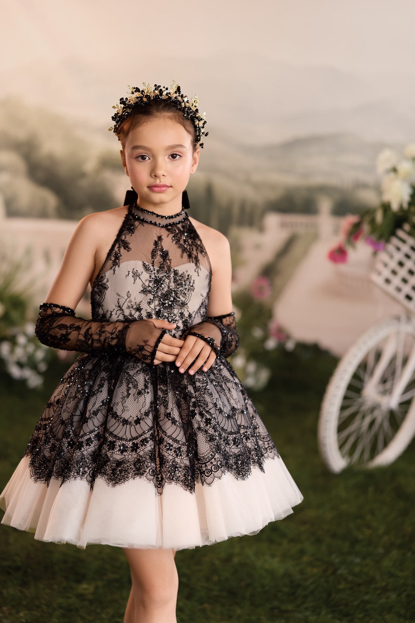 Girl wearing a black lace halter dress with matching gloves and a decorative gold and black headpiece | Girls Formal Dress