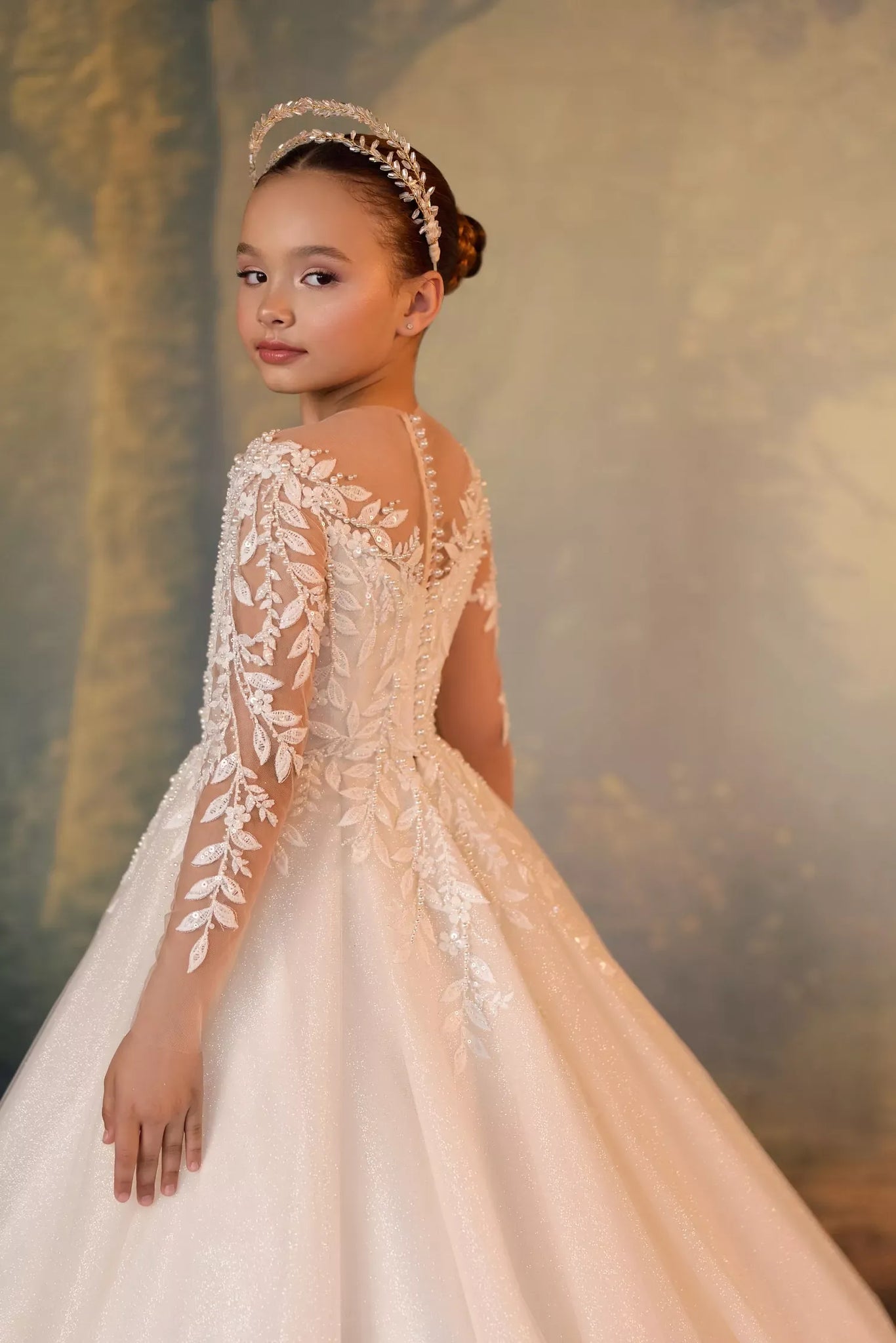 Girl wearing a white long sleeve ball gown with leaf embroidery and a pearl headband