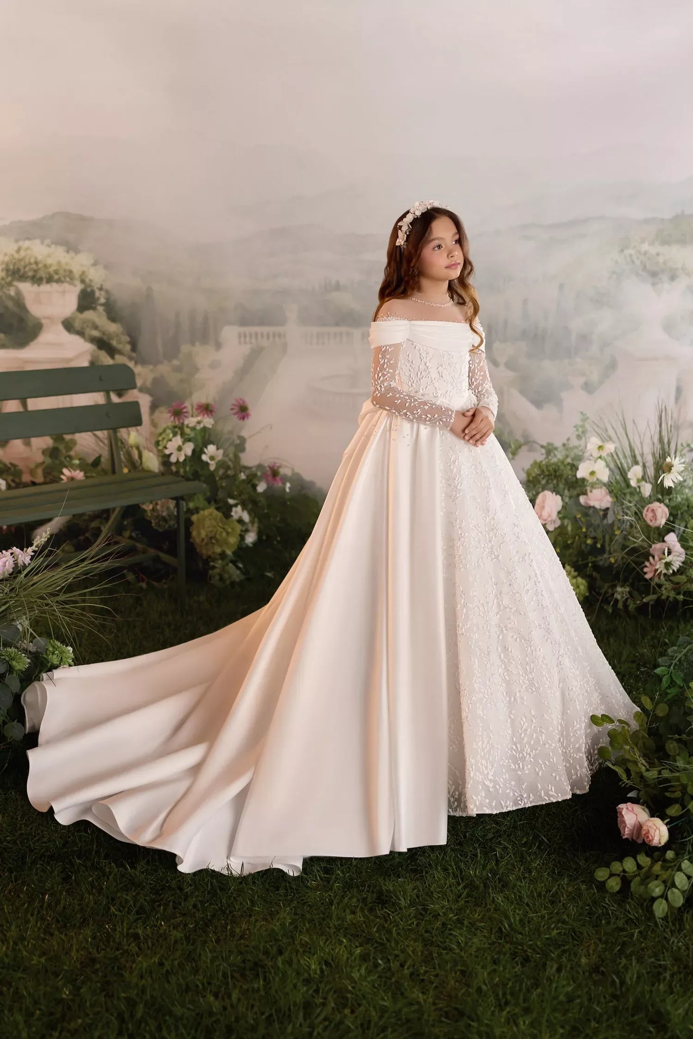 Girl wearing a white off the shoulder ball gown with lace sleeves and a long train in a garden setting