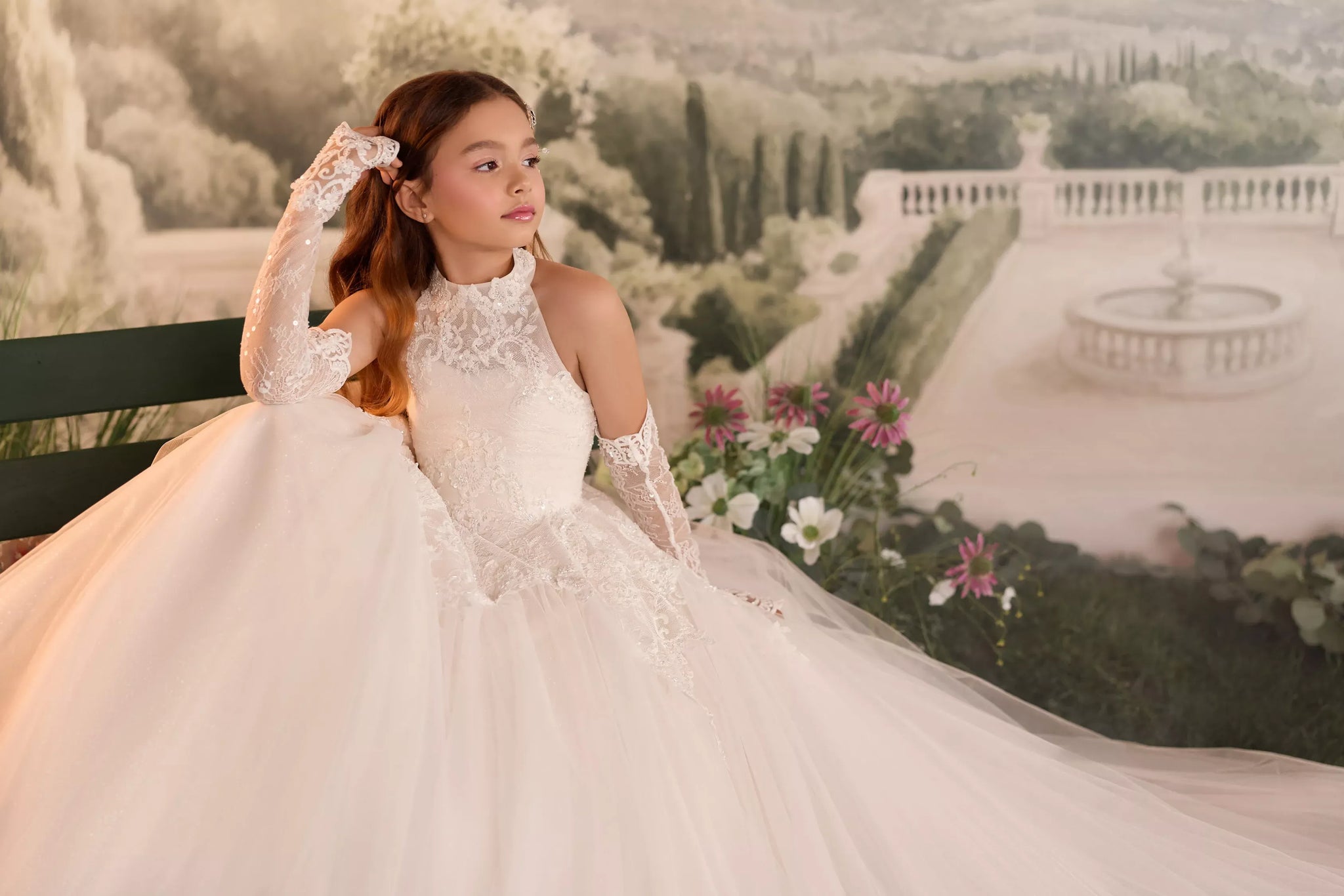 Girl wearing a white lace high neck ball gown with matching lace gloves sitting on a bench | Girls Formal Dress