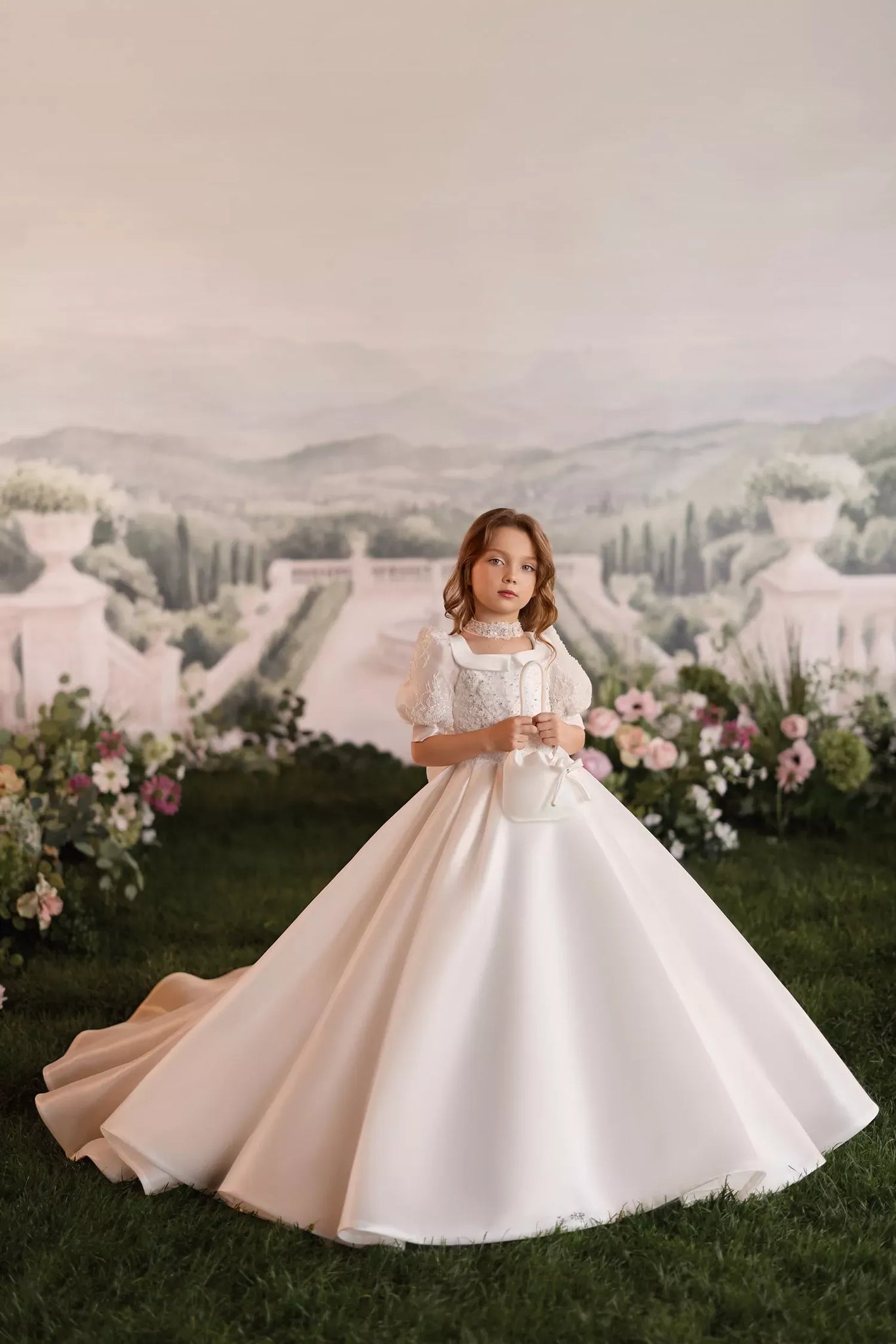 Girl wearing a white ball gown with puff sleeves and a lace collar holding a small white handbag | Girls Formal Dress