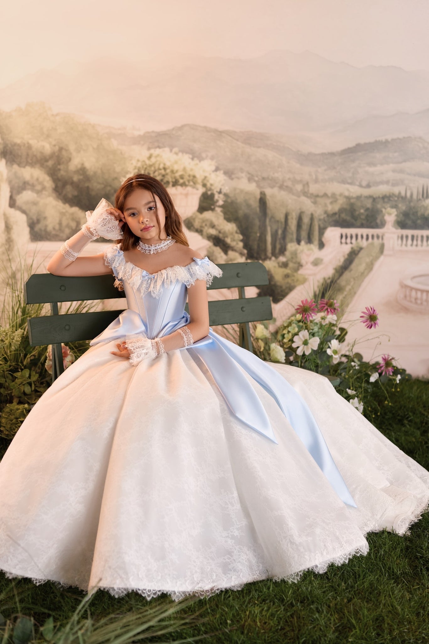 Girl wearing a blue and white lace ball gown with matching lace gloves sitting on a bench
