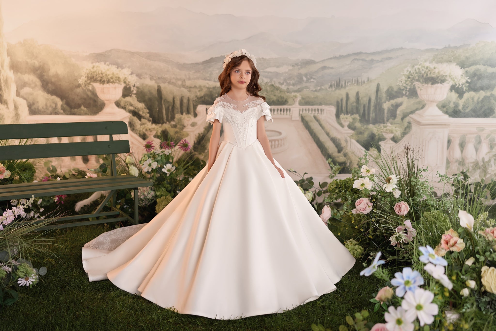 Girl wearing a white formal dress with a floral headband standing in a garden setting