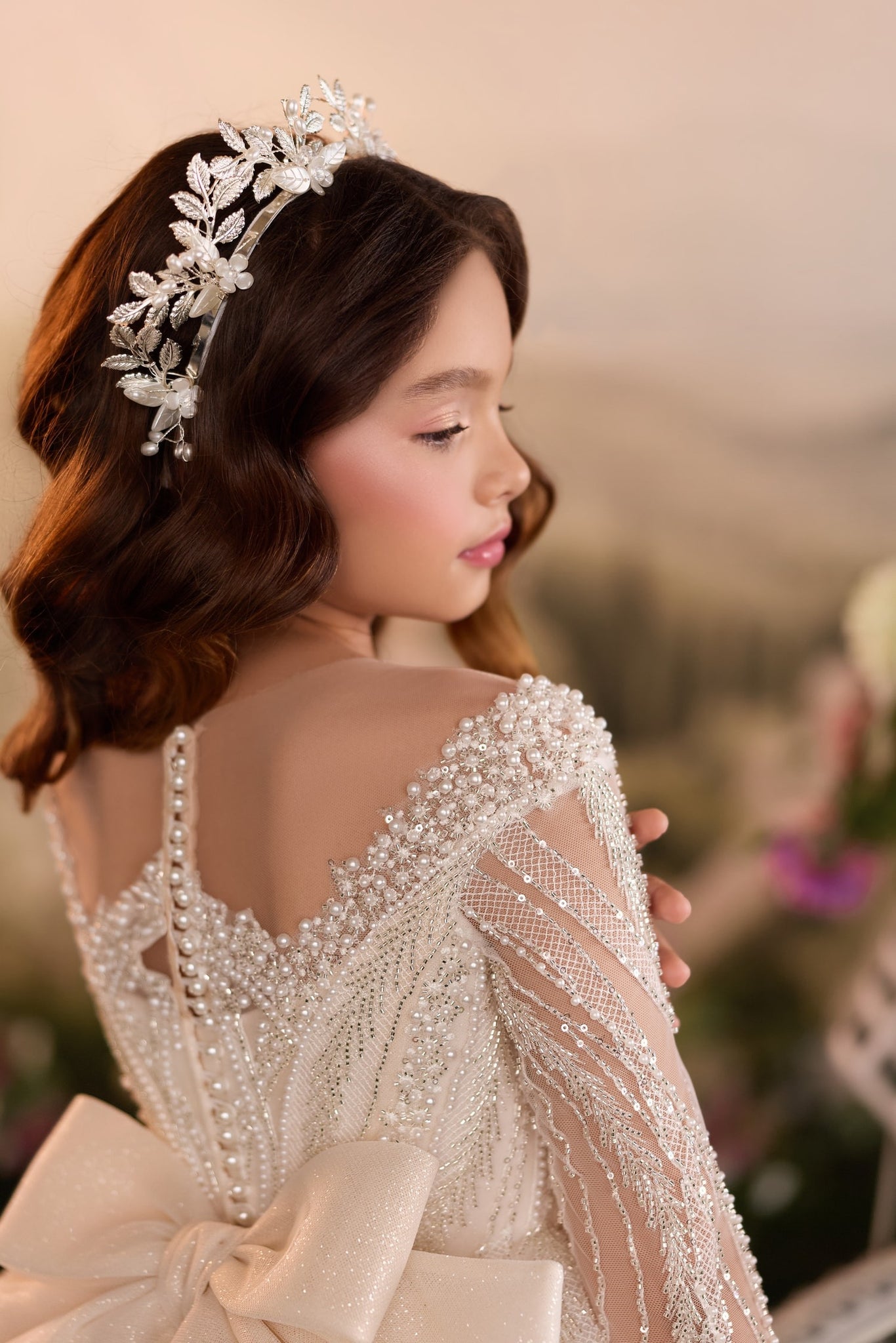 Girl wearing a pearl and sequin embellished dress with a matching floral headpiece