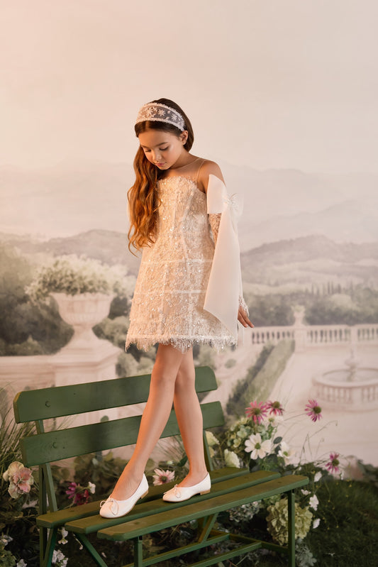 Girl wearing a white lace dress and headband standing on a green garden bench