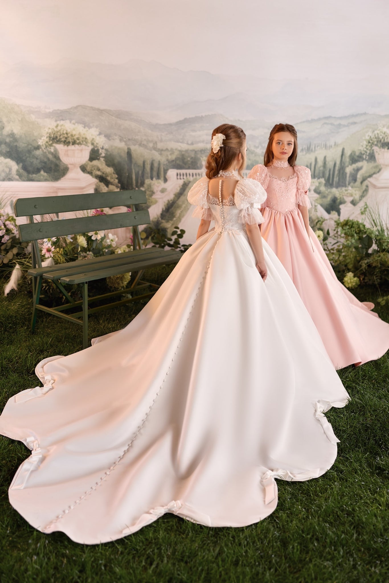 Two girls wearing formal ball gowns standing in a garden setting