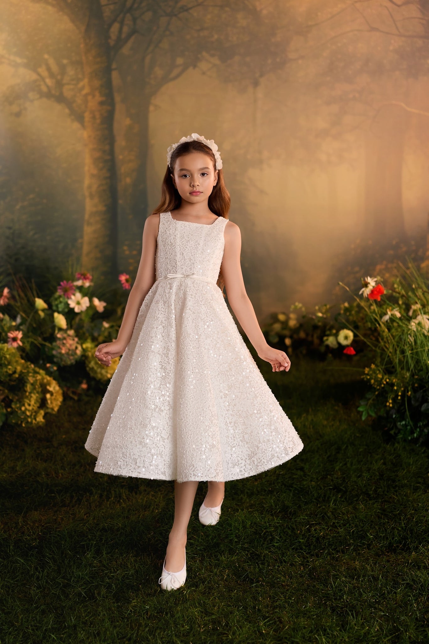 Girl wearing a white sequined sleeveless dress and floral headband in a garden setting