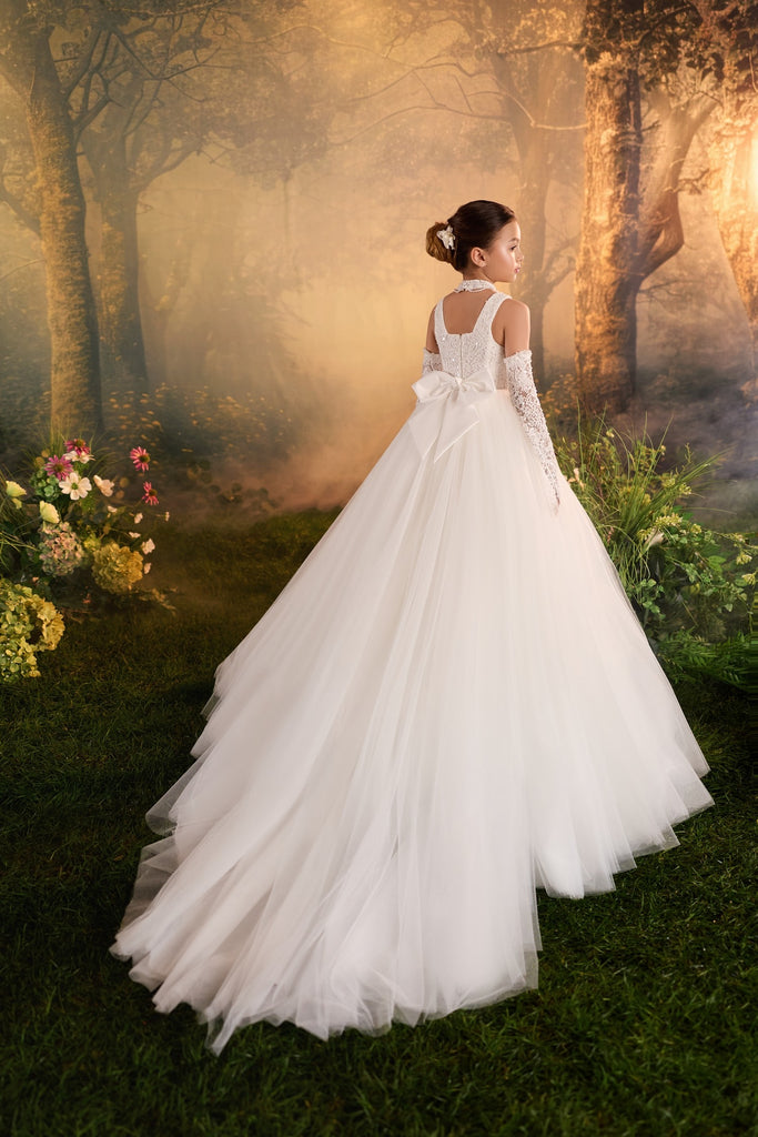 Girl wearing a white floor length tulle dress with a bow and lace gloves in a forest setting | Girls Formal Dress
