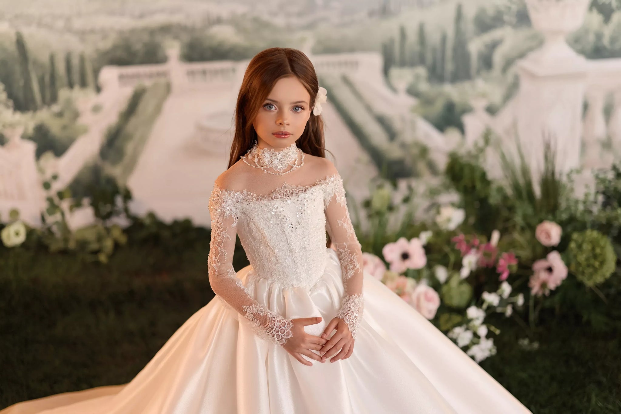 Girl wearing a white off the shoulder lace ball gown with long sleeves and a pearl choker