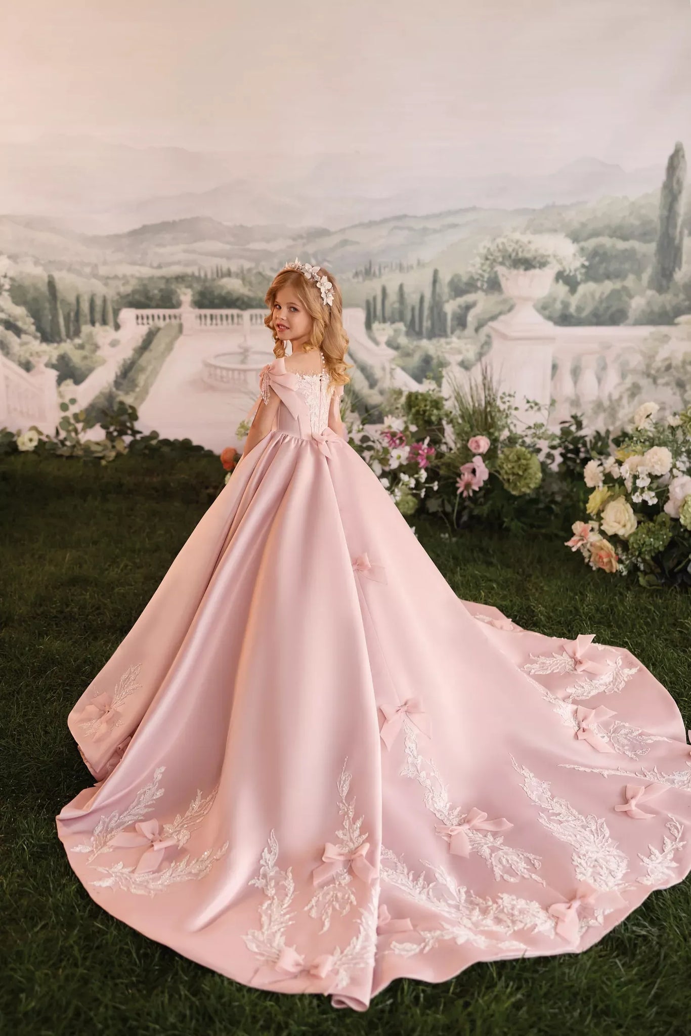 Girl wearing a pink ball gown with a long train and floral embroidery standing in a garden