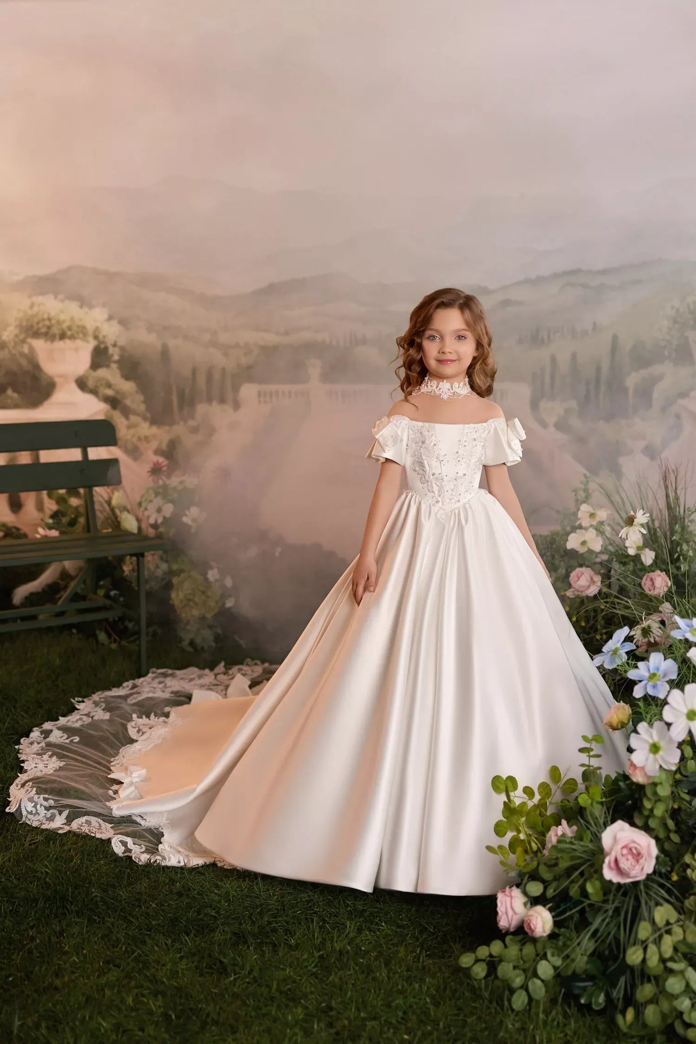 Girl wearing a white off-shoulder ball gown with lace details and a long train in a garden setting