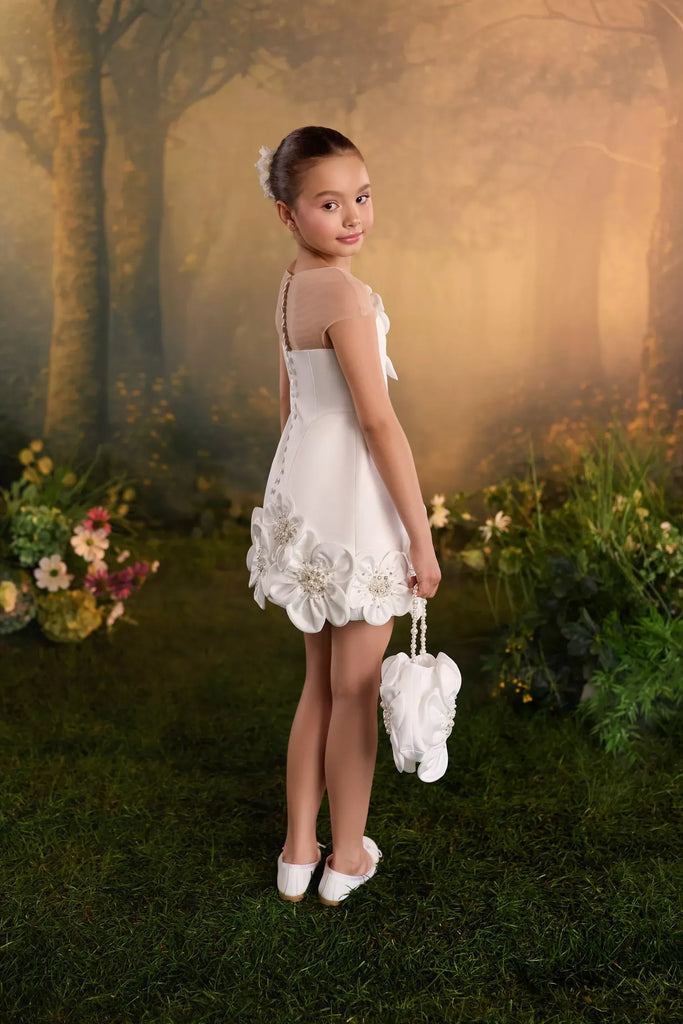 Girl wearing a white sleeveless dress with floral hem details and holding a small matching bag | Girls Formal Dress