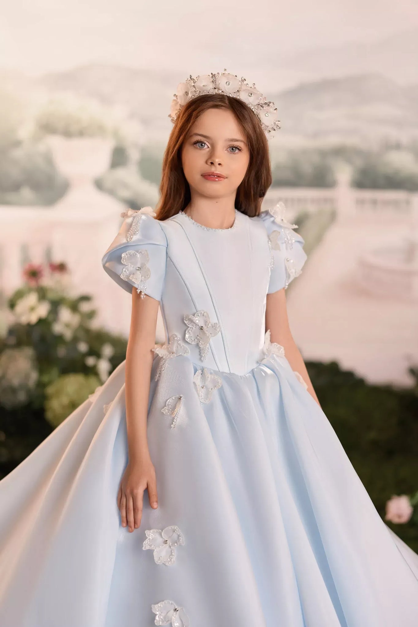 Girl wearing a light blue ball gown with floral embellishments and a matching tiara