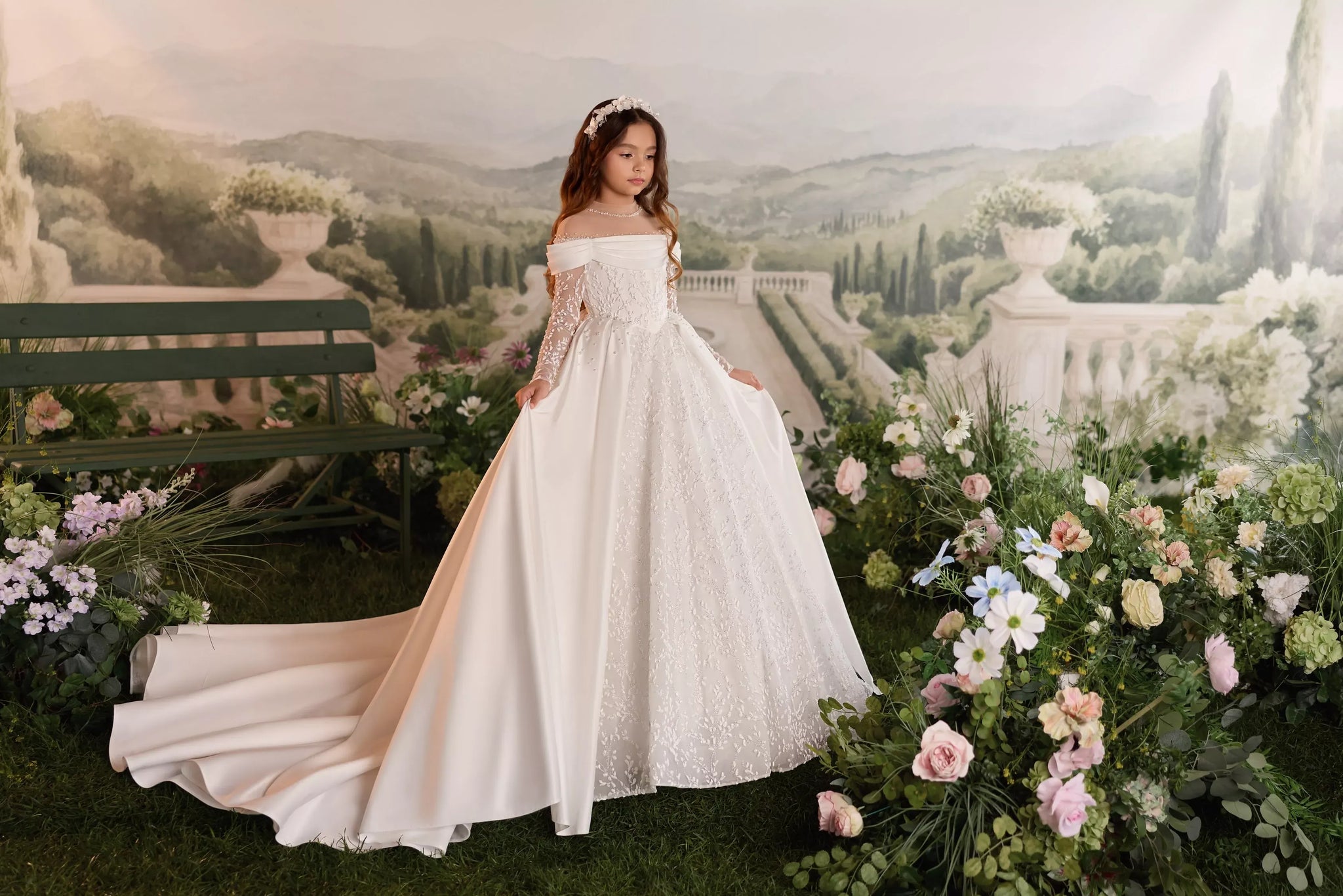 Girl wearing a white off-shoulder ball gown with lace sleeves and a long train in a garden setting
