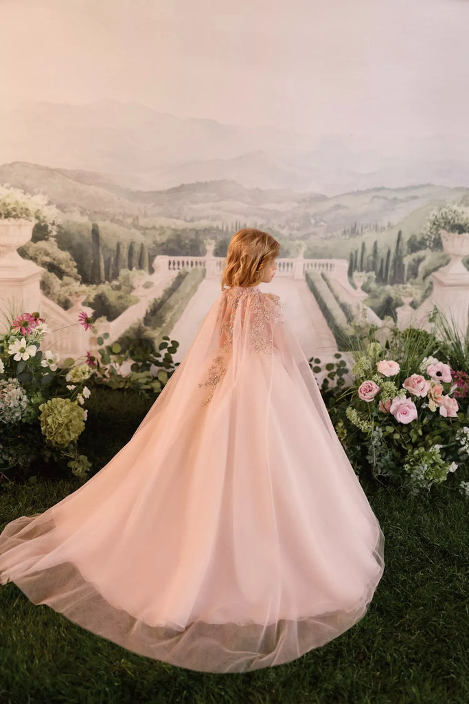 Child wearing a long pink tulle dress with lace detail standing in front of a garden backdrop | Girls Formal Dress