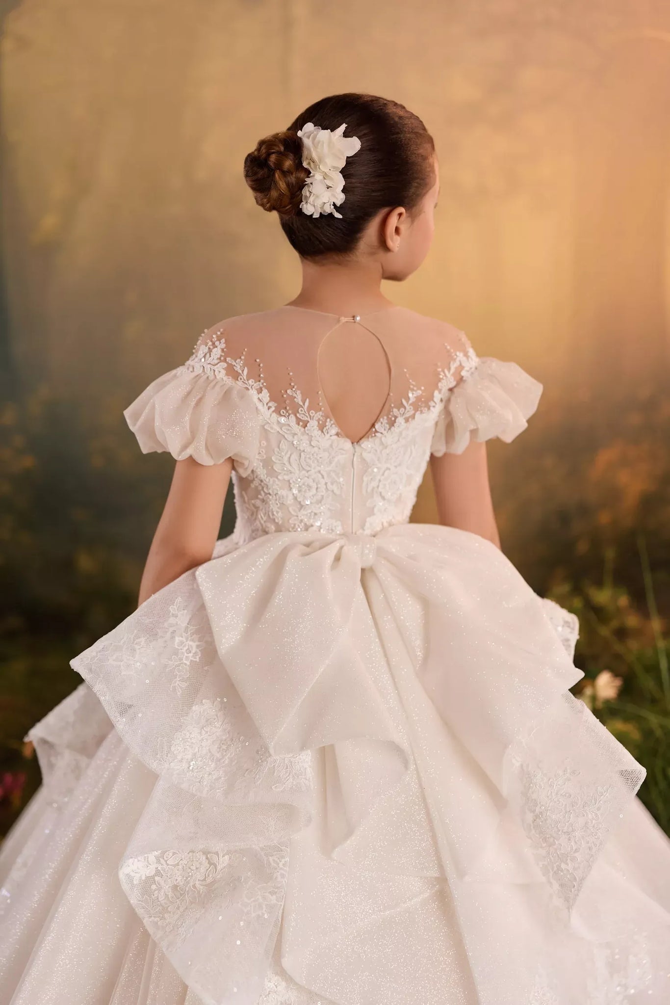 Back view of a girl wearing a white lace dress with puff sleeves and a large bow